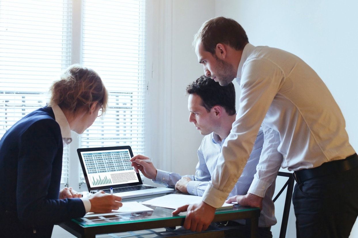 Business team analyzing data on a laptop showing spreadsheets and charts during an office meeting.