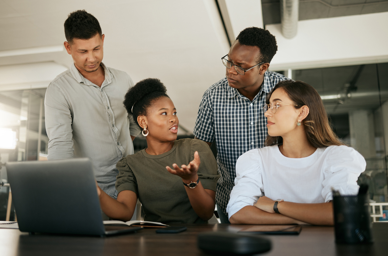Four coworkers having a discussion around a laptop in an office.